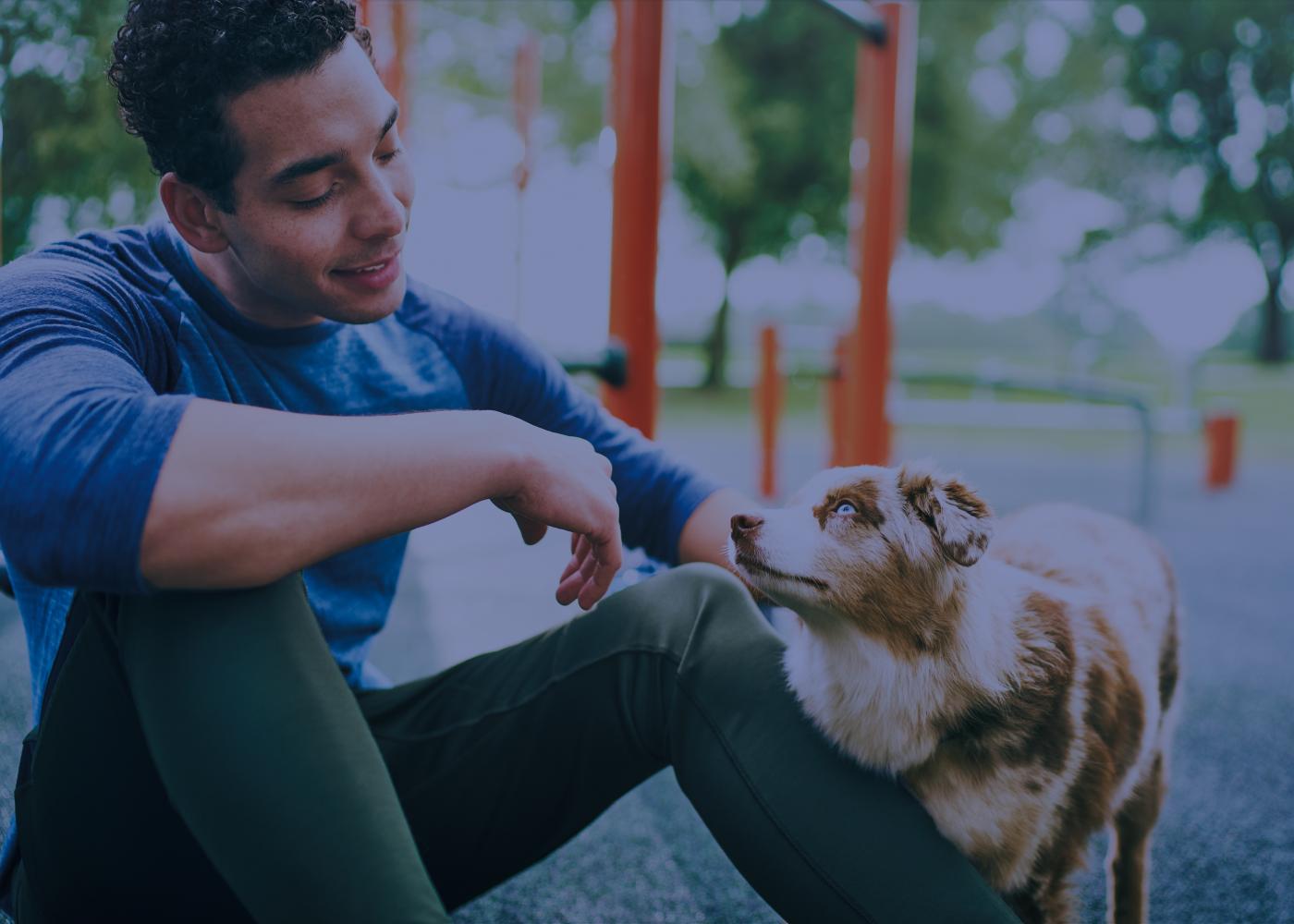 Man sitting by playground petting Australian Shepherd