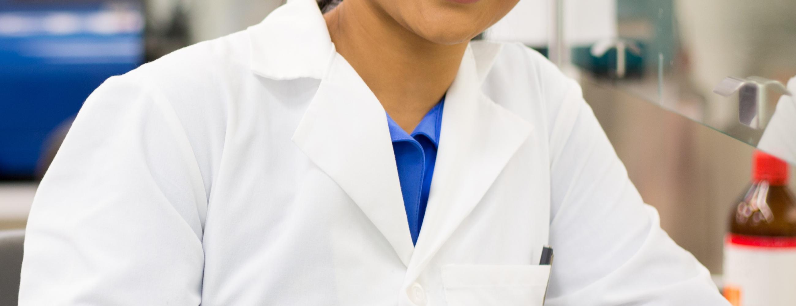 Young woman in labcoat and gloves smiling at the camera in a lab setting